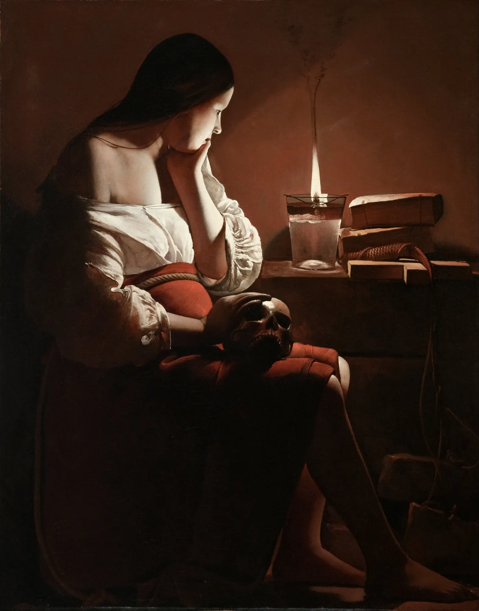 A young woman sits in profile in a pitch-dark room, a skull resting on her lap, her face lit only by the single smoking flame of an oil lamp she watches.